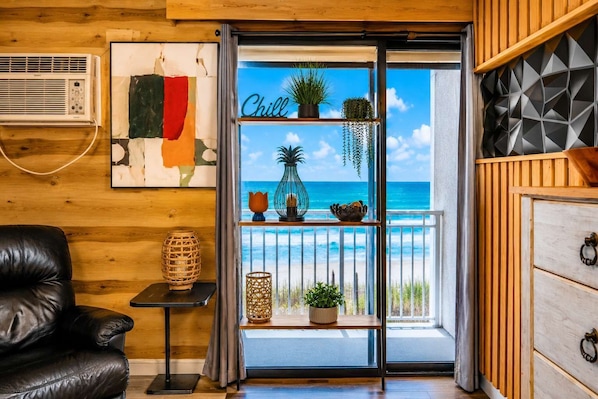 Ein Zimmer mit Holzvertäfelung, einem schwarzen Ledersessel, einem kleinen Tisch mit Dekoration und Meerblick durch eine Glastür. Auf der Tür ist ein Schild mit der Aufschrift 'Chill'.