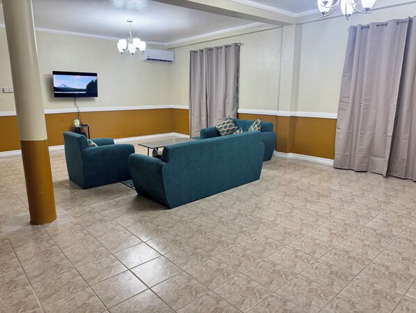 Un salón con sofás color turquesa, un televisor de pantalla plana, una araña y un piso con baldosas.