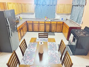 Una cocina con armarios de madera, un refrigerador, una estufa y una mesa de comedor con sillas.