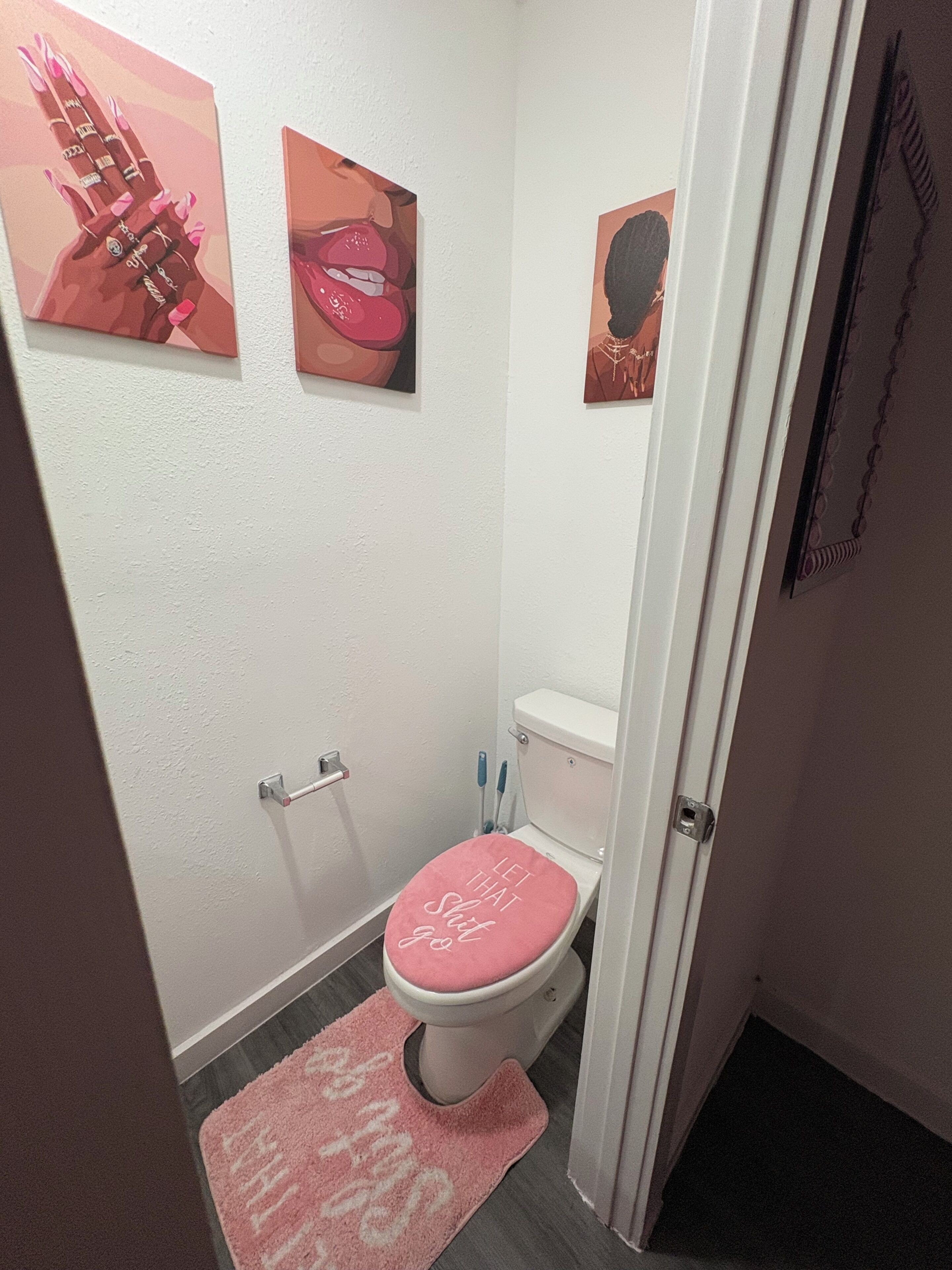 Ein Badezimmer mit Toilette, einer rosa Fußmatte und drei Bildern an der Wand.