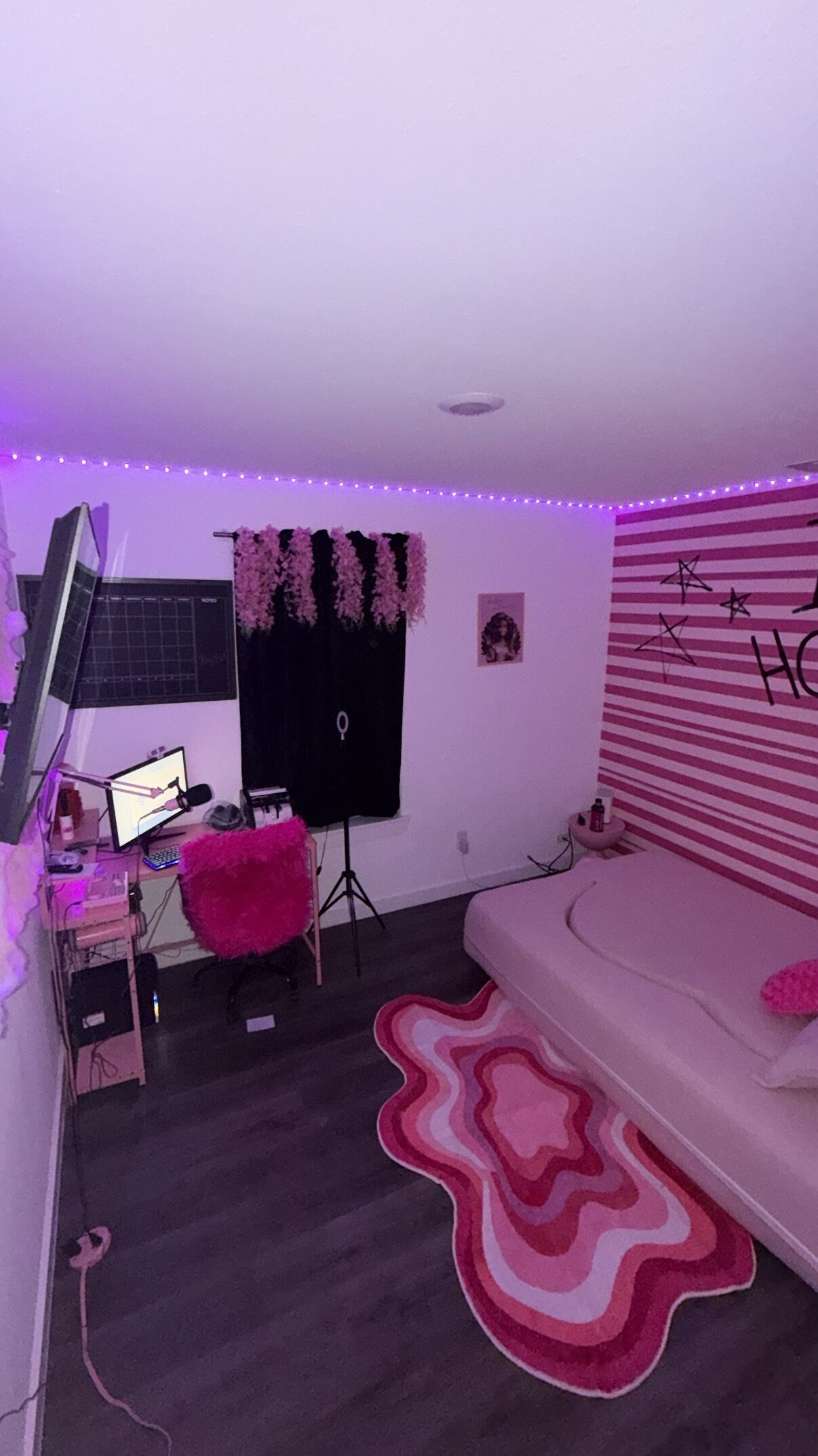 A room with a desk, computer, and a bed with a pink pillow.