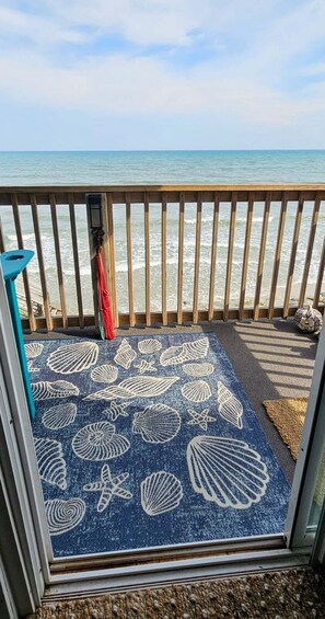 Ein Balkon mit Meerblick, eine blaue Matte mit Muschelmuster, ein Holgitter und ein kleiner blauer Stuhl.
