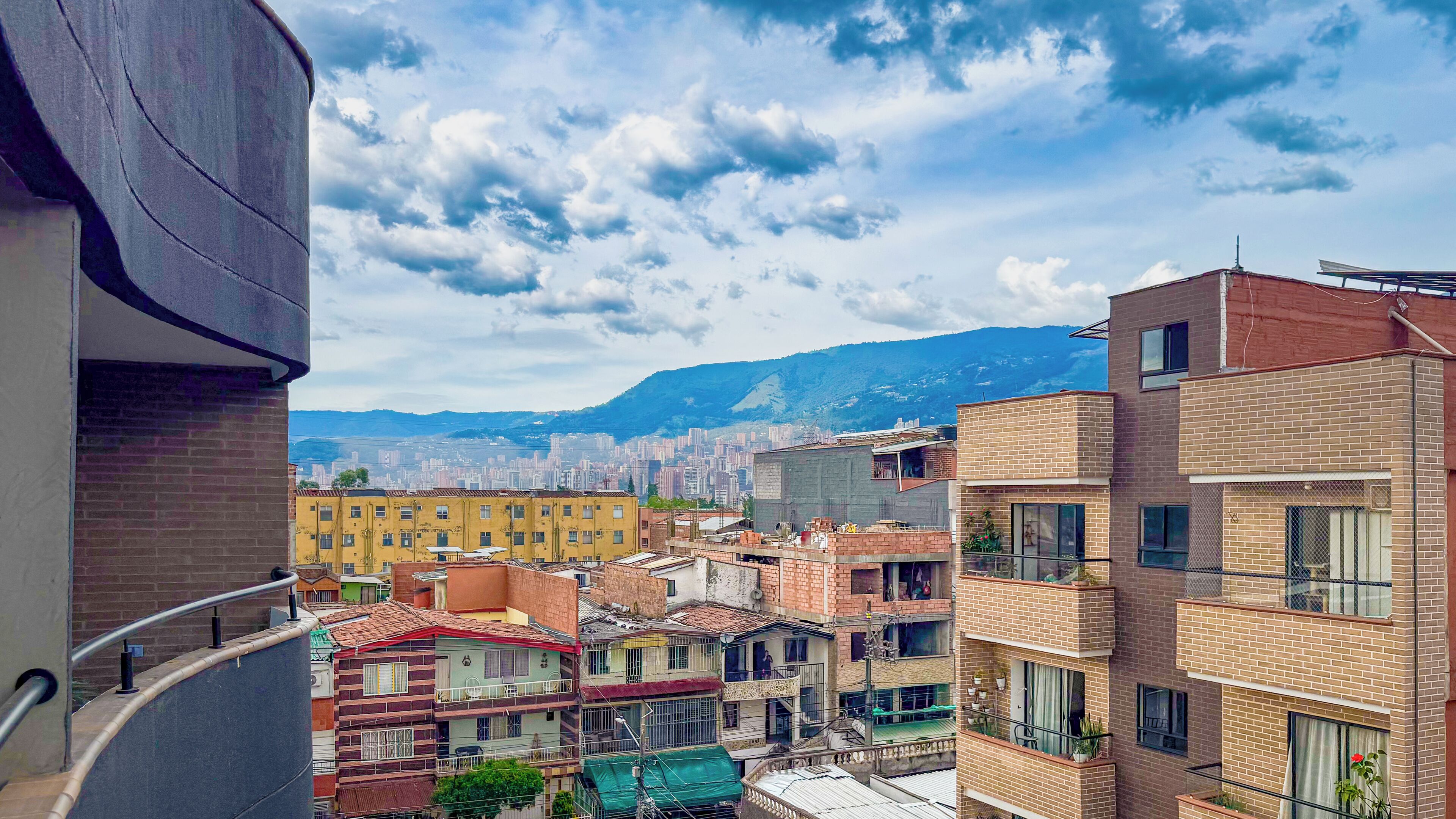 A residential area with multi-story buildings, some with balconies, and a mountainous backdrop.