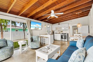 A spacious living area with a ceiling fan, a sofa, a coffee table, and a kitchen in the background. - Reel-Axed Retreat ~ Pet Friendly, 37.5' Dock, Tiki Hut, Cabana Club w Pool Access (Key Colony Beach)