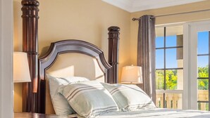 A bed with a wooden headboard, two bedside lamps, and a view of greenery through a window.