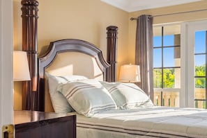 A bed with a wooden headboard, two bedside lamps, and a view of greenery through a window.