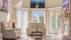 A spacious living room with a reclining chair, a sofa, a glass coffee table, and large windows with blinds.