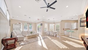 A spacious living room with a ceiling fan, a dining area with a white table and chairs, and a kitchen with white cabinets and a countertop.