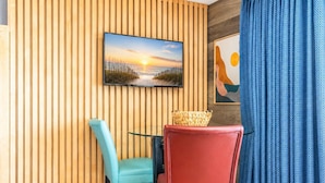 Habitación con pared de listones de madera, un televisor sobre una mesa con dos sillas y una cortina azul.
