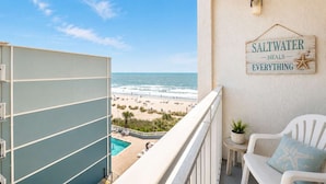 Un balcón con vistas a la playa, un letrero que dice 'Saltwater heals everything', una mesita con una planta y una silla blanca con un cojín de estrella de mar.