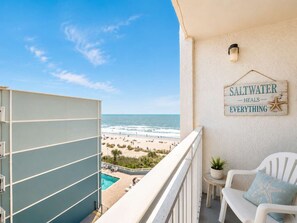 Ein Balkon mit Blick auf den Strand, ein Schild mit der Aufschrift 'Saltwater heals everything', ein kleiner Tisch mit einer Pflanze und ein weißer Stuhl mit Kissen in Form eines Seesterns.