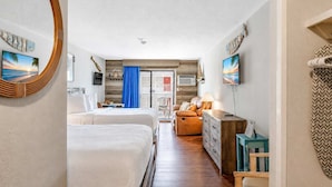 Habitación de hotel con dos camas, un sofá, un televisor y vista al mar.