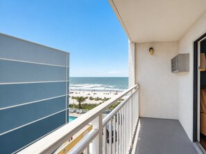 Ein Balkon mit Blick auf Strand und Meer, ein weißes Geländer und ein kleiner Poolbereich.