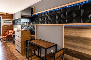 Ein modernes Zimmer mit Schreibtisch aus Holz, einem Sessel, einem Flachbildfernseher und einer Wand mit geometrischem Muster.