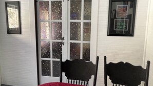 Une pièce avec un mur blanc, une porte dotée de panneaux en verre dépoli, deux chaises noires et une table rouge.