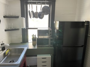 Una cucina con un lavello in acciaio inossidabile, un frigorifero nero, un forno tostatutto e pentole appese.