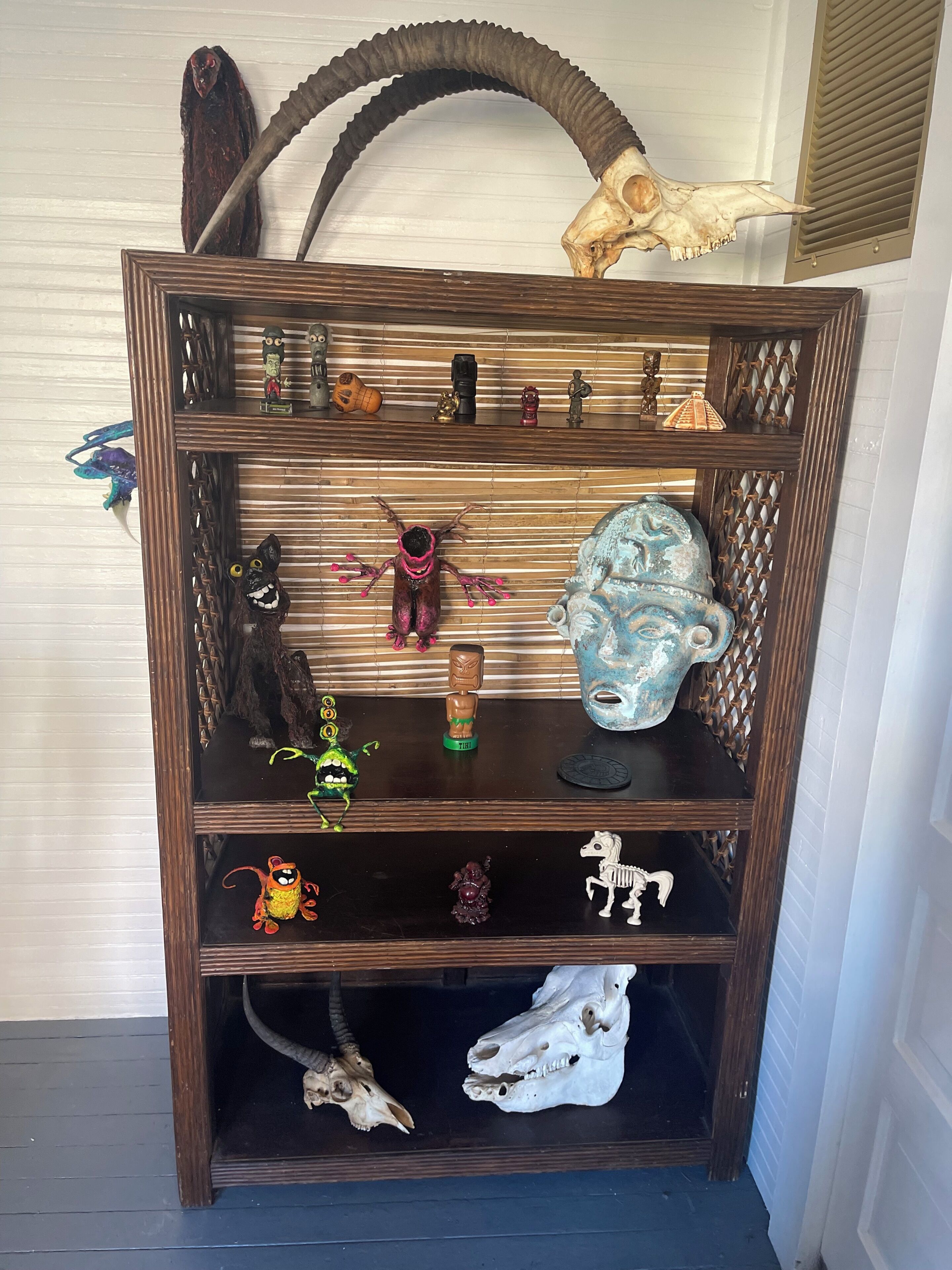 Une étagère en bois servant d’élément de décoration, sur laquelle sont disposés divers objets, notamment des figurines, un crâne et un masque.
