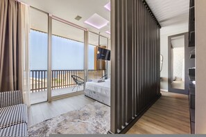 A modern hotel room with a balcony, a bed, a TV, and a wooden floor. - Luxe Green Coast Villa Jacuzzi Free Buggy (Himarë)