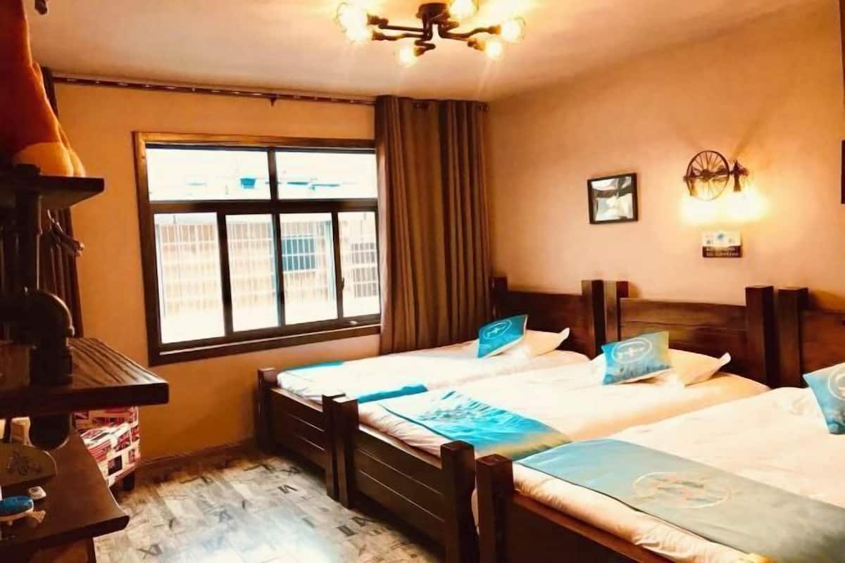 A hotel room with two beds, a desk, a window with curtains, and a wall-mounted light fixture.