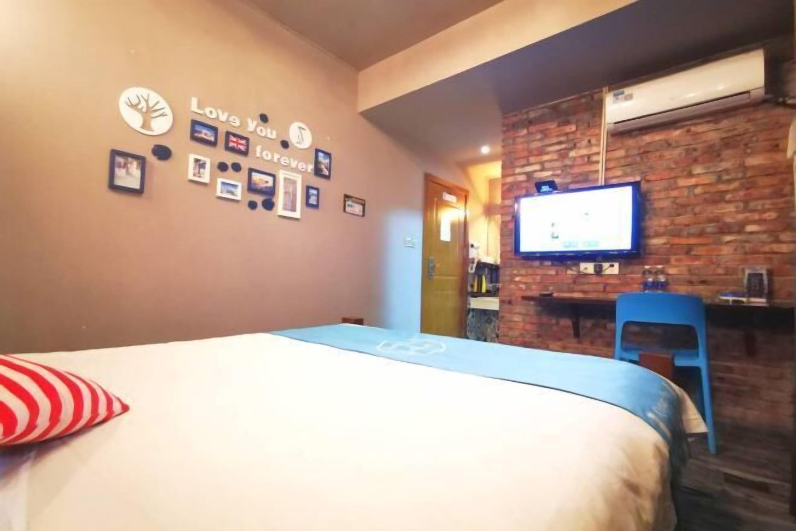Quarto de hotel com uma cama, televisão presa a uma parede de tijolos e uma pequena mesa com uma cadeira.