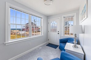 A room with large windows, a door, a blue sofa, a white table, and a lamp. - Amazing Beach House with Ocean Views - Just steps to Wells Beach (Wells)
