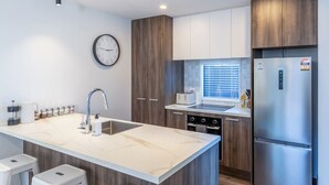 A modern kitchen with a marble countertop, stainless steel appliances, wooden cabinets, and a built-in oven. - Family Friendly Home near Fitzgerald Ave + Garage (Christchurch)