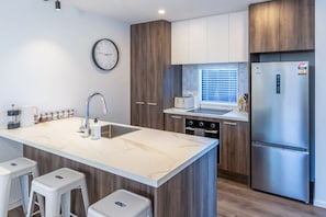Eine moderne Küche mit Marmorarbeitsplatte, Edelstahlgeräten, Holzschränken und einem eingebauten Backofen.