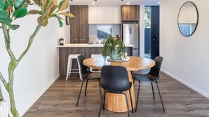 A modern kitchen with wooden cabinets, a stainless steel refrigerator, and a dining area with a round wooden table and black chairs. - Family Friendly Home near Fitzgerald Ave + Garage (Christchurch)