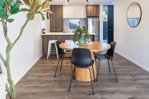 Eine moderne Küche mit Holzschränken, einem Edelstahlkühlschrank und einem Essbereich mit einem runden Holztisch und schwarzen Stühlen.