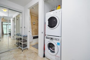 A laundry area with a front-loading washer and dryer, a glass door leading to a bathroom, and a metal rack with folded towels. - Urban 1BR Escape with Queen Bed in Prime Toronto Location (Toronto)