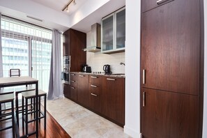 A modern kitchen with dark wooden cabinets, a gas stove, and a built-in oven. There is a dining area with a table and chairs, and a window with blinds. - Urban 1BR Escape with Queen Bed in Prime Toronto Location (Toronto)