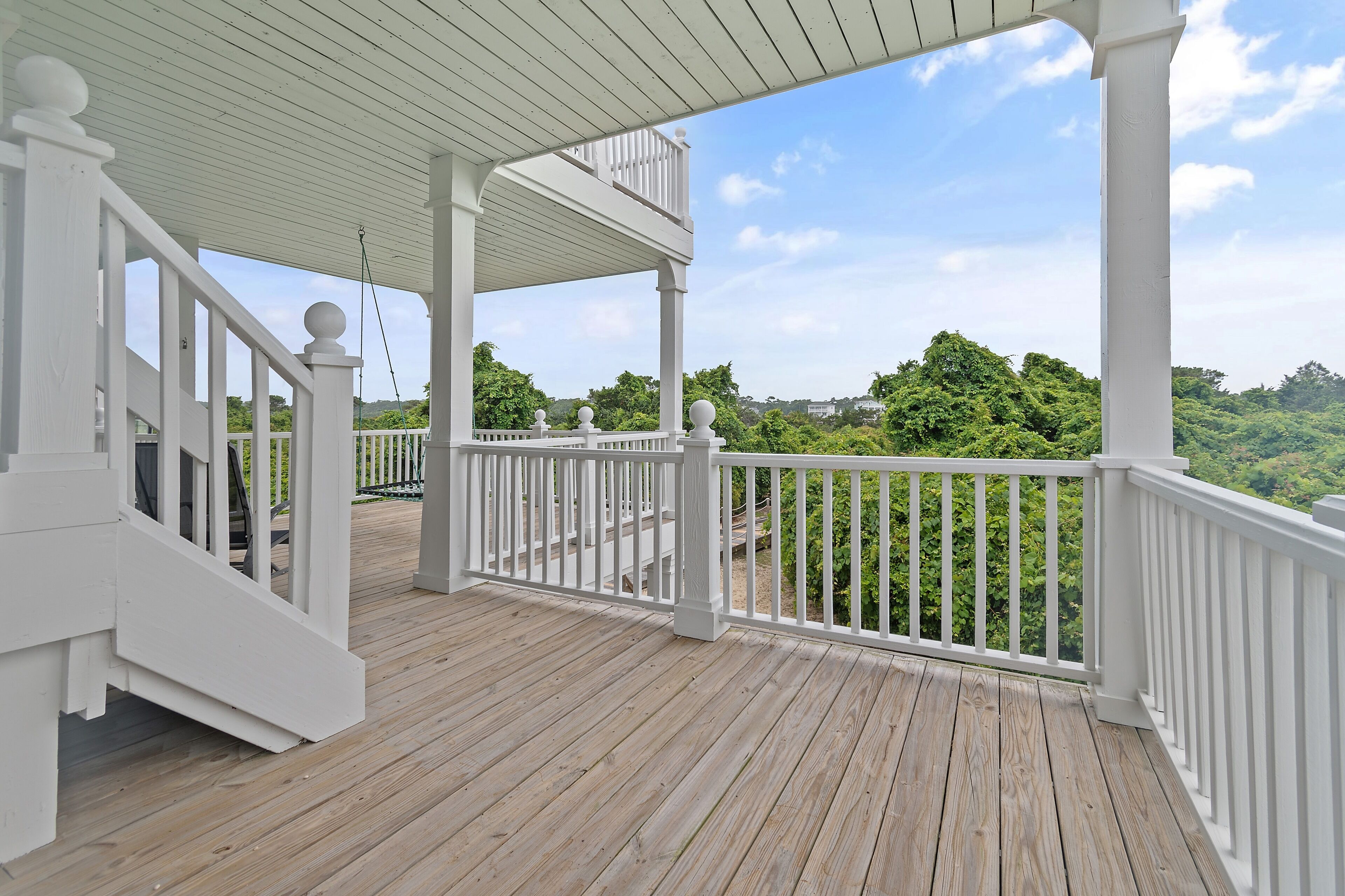 A wooden deck with white railings and a staircase leading to an upper level.