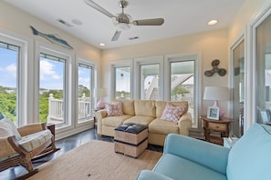 A spacious living room with a large window, a ceiling fan, and a view of the outdoors. - "Escape" 5 Bedrooms, 6.5 Bathrooms, ICW Home, Community Pool and Tennis Court! (Supply)