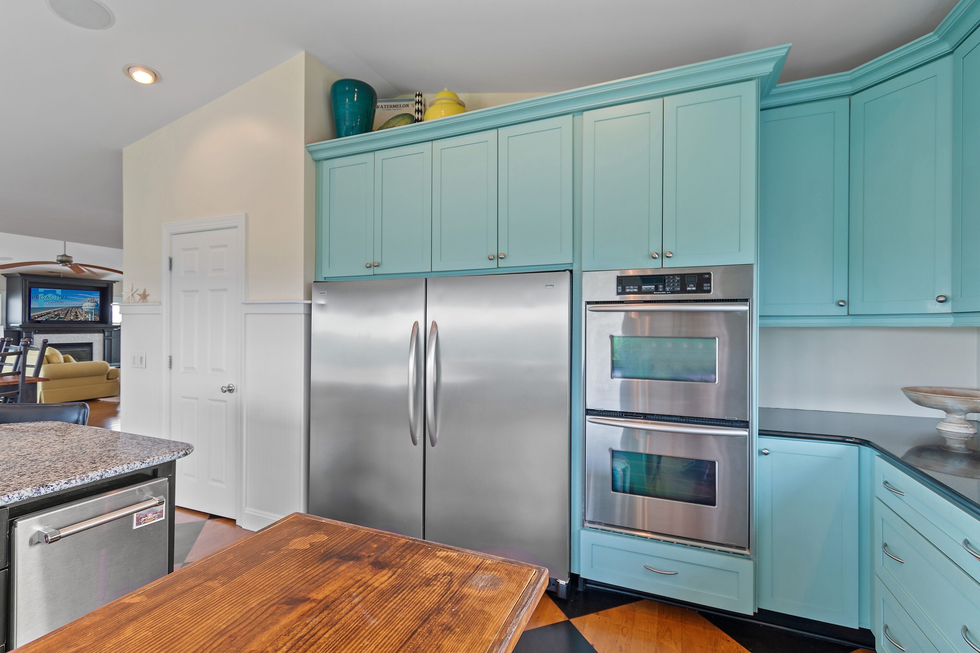 A kitchen with teal cabinets, stainless steel appliances, and a wooden dining table.