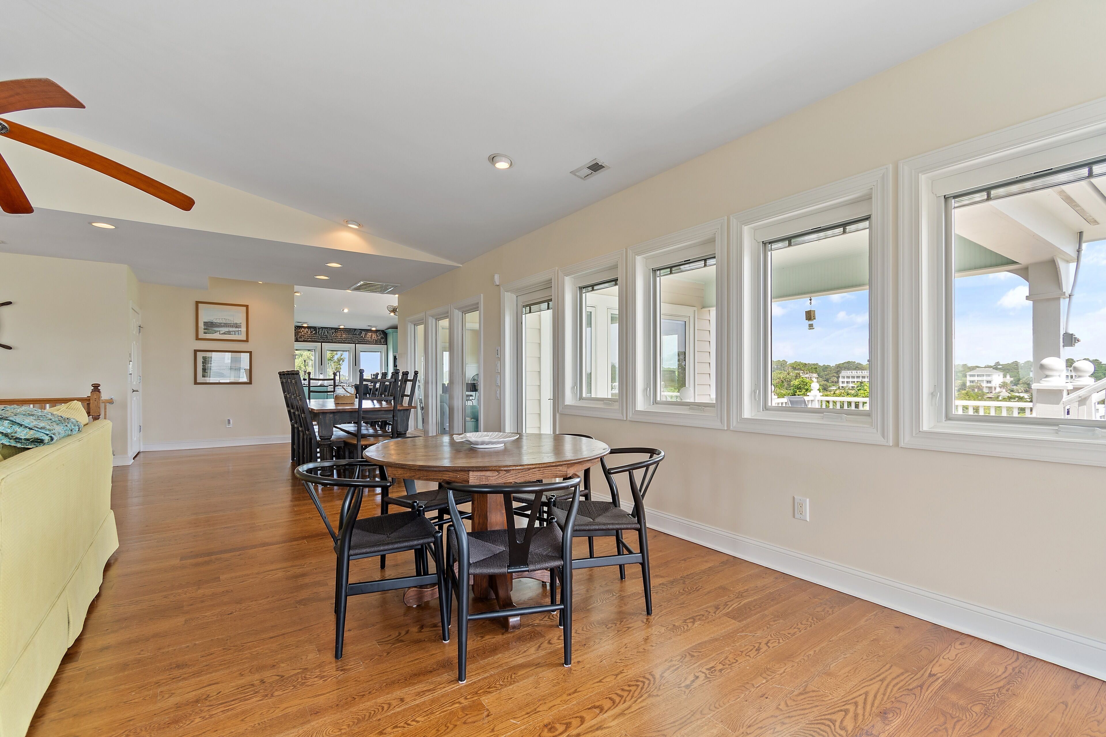 A dining area with a round table and chairs, large windows, and hardwood flooring.