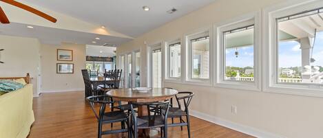 A dining area with a round table and chairs, large windows, and hardwood flooring.