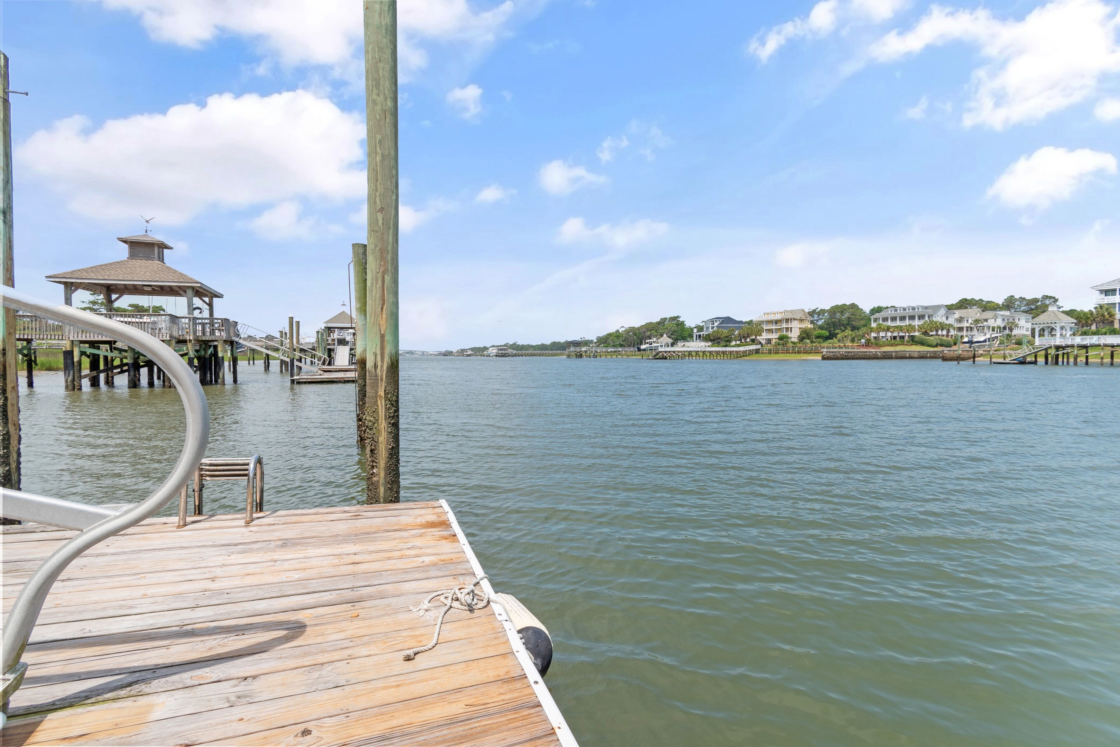 A wooden dock extending into calm water, a gazebo-like structure, and a distant shoreline with buildings.