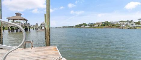 A wooden dock extending into calm water, a gazebo-like structure, and a distant shoreline with buildings.