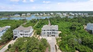 A large, multi-story house with a spacious front yard, a dock, and a lake view. - "Escape" 5 Bedrooms, 6.5 Bathrooms, ICW Home, Community Pool and Tennis Court! (Supply)