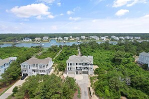 A large, multi-story house with a spacious front yard, a dock, and a lake view. - "Escape" 5 Bedrooms, 6.5 Bathrooms, ICW Home, Community Pool and Tennis Court! (Supply)