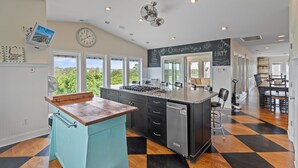 A kitchen with a central island, a dining area with a table and chairs, and a view of greenery outside. - "Escape" 5 Bedrooms, 6.5 Bathrooms, ICW Home, Community Pool and Tennis Court! (Supply)