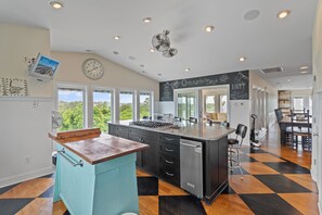 A kitchen with a central island, a dining area with a table and chairs, and a view of greenery outside. - "Escape" 5 Bedrooms, 6.5 Bathrooms, ICW Home, Community Pool and Tennis Court! (Supply)