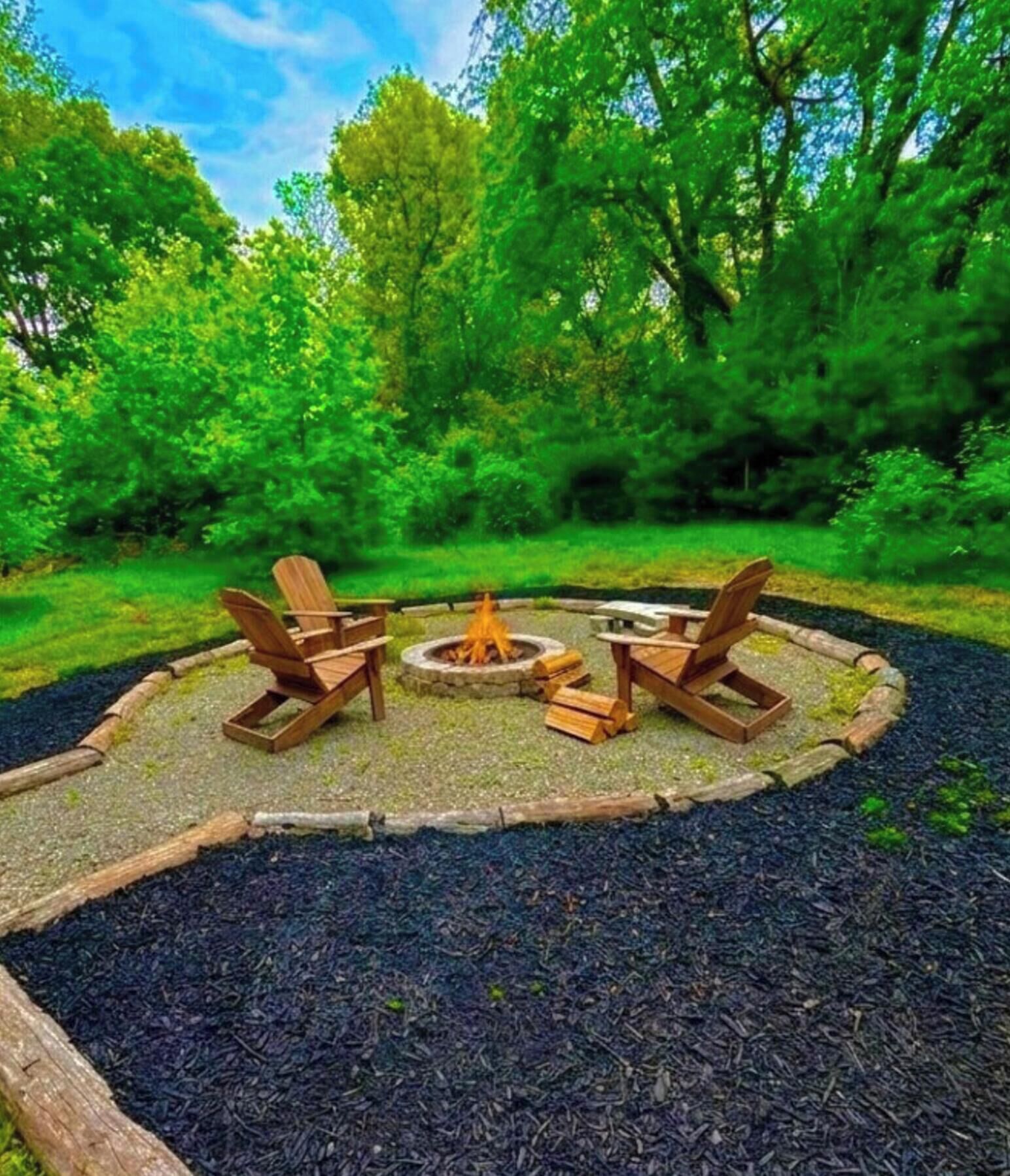 A circular outdoor seating area with a fire pit, surrounded by a wooden fence and a gravel path.