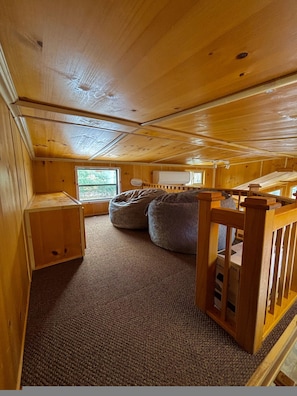 Interior de una cabaña con techo de madera, una ventana, una cama y un pequeño rincón de escritorio.