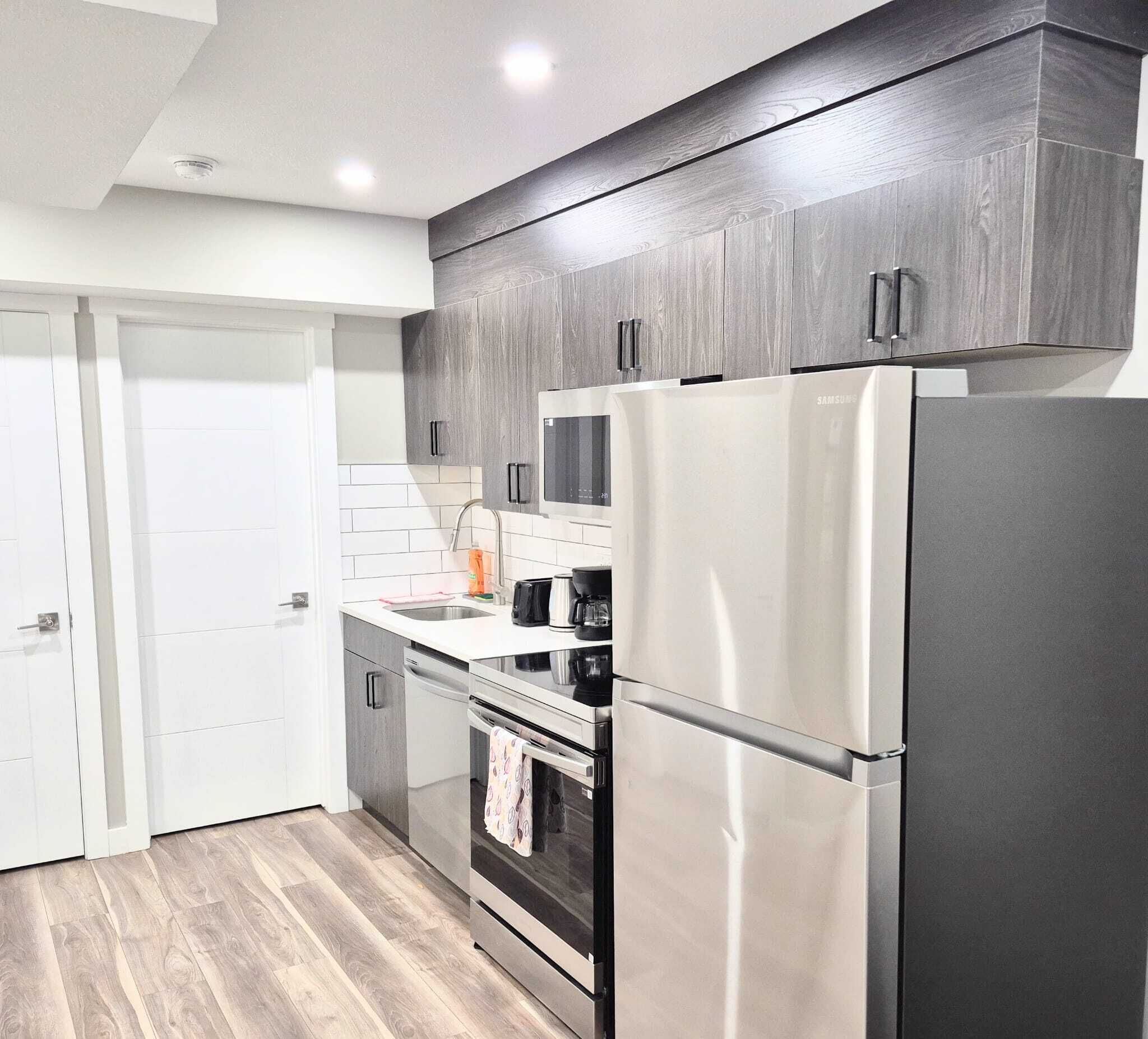 A modern kitchen with stainless steel appliances, a white tiled backsplash, and dark wood cabinets.