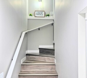 Eine Treppe mit Holzbodenstufen und einem weißen Geländer, die zu einer Empfangsebene mit einem motivierenden Schild und kleinen Pflanzen führt.