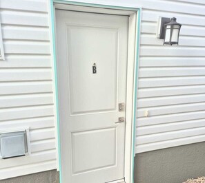 Eine weiße Tür mit einem 'B' auf dem Schild, ein Briefkasten und eine Wandleuchte.
