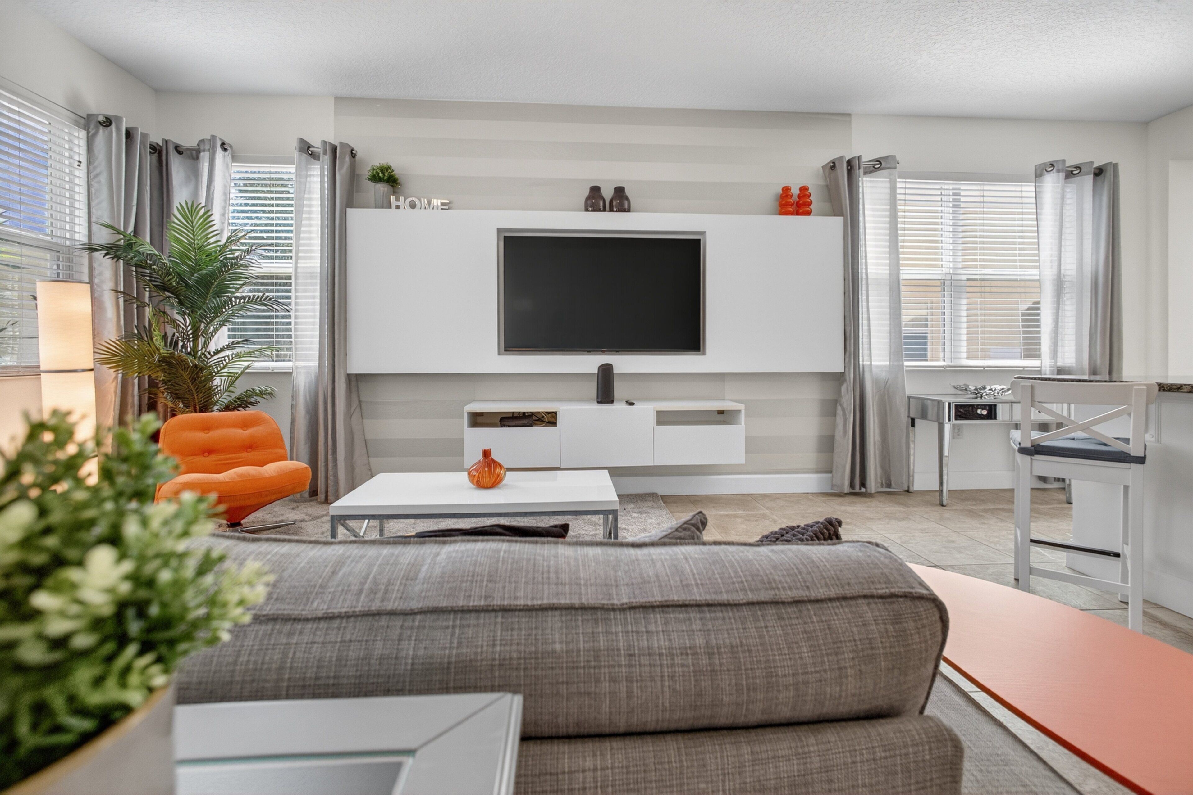 A modern living room with a grey sofa, white coffee table, and a flat-screen TV mounted on the wall.