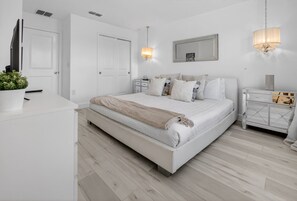 Ein modernes Schlafzimmer mit einem großen Bett, Nachttischen, einem Spiegel und einer Chandelüster.