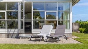A modern house with large windows, a patio with two lounge chairs, and a visible interior with a dining area. - Gorgeous home in Otterup with WiFi (Otterup)